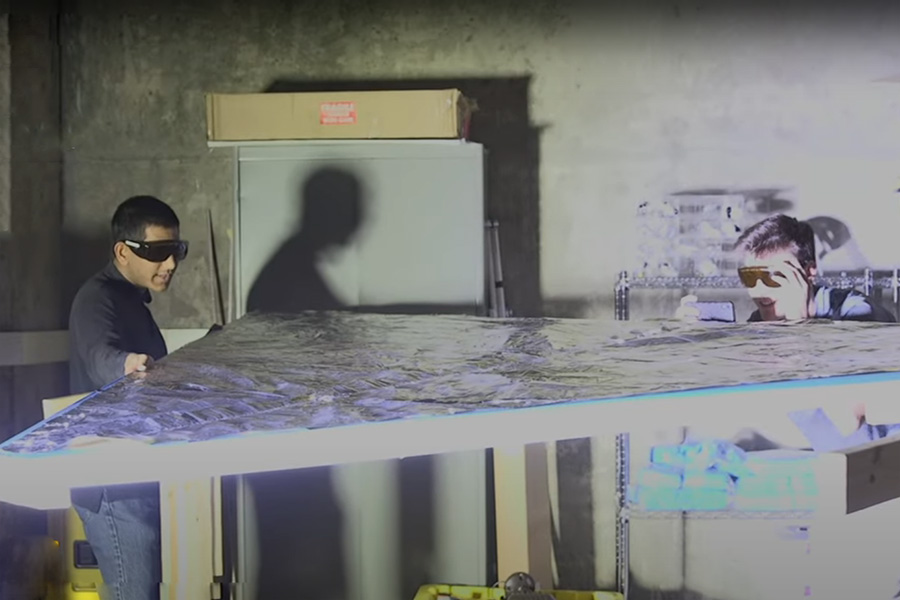 Two students wearing safety glasses and looking closely at a reflective sheet in bright light