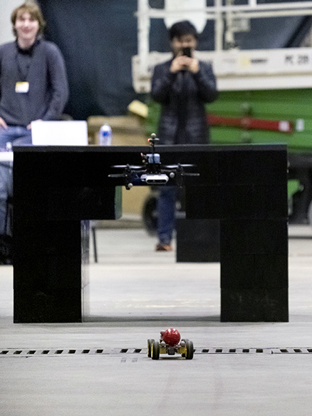 an drone follows a small car on a concrete floor.