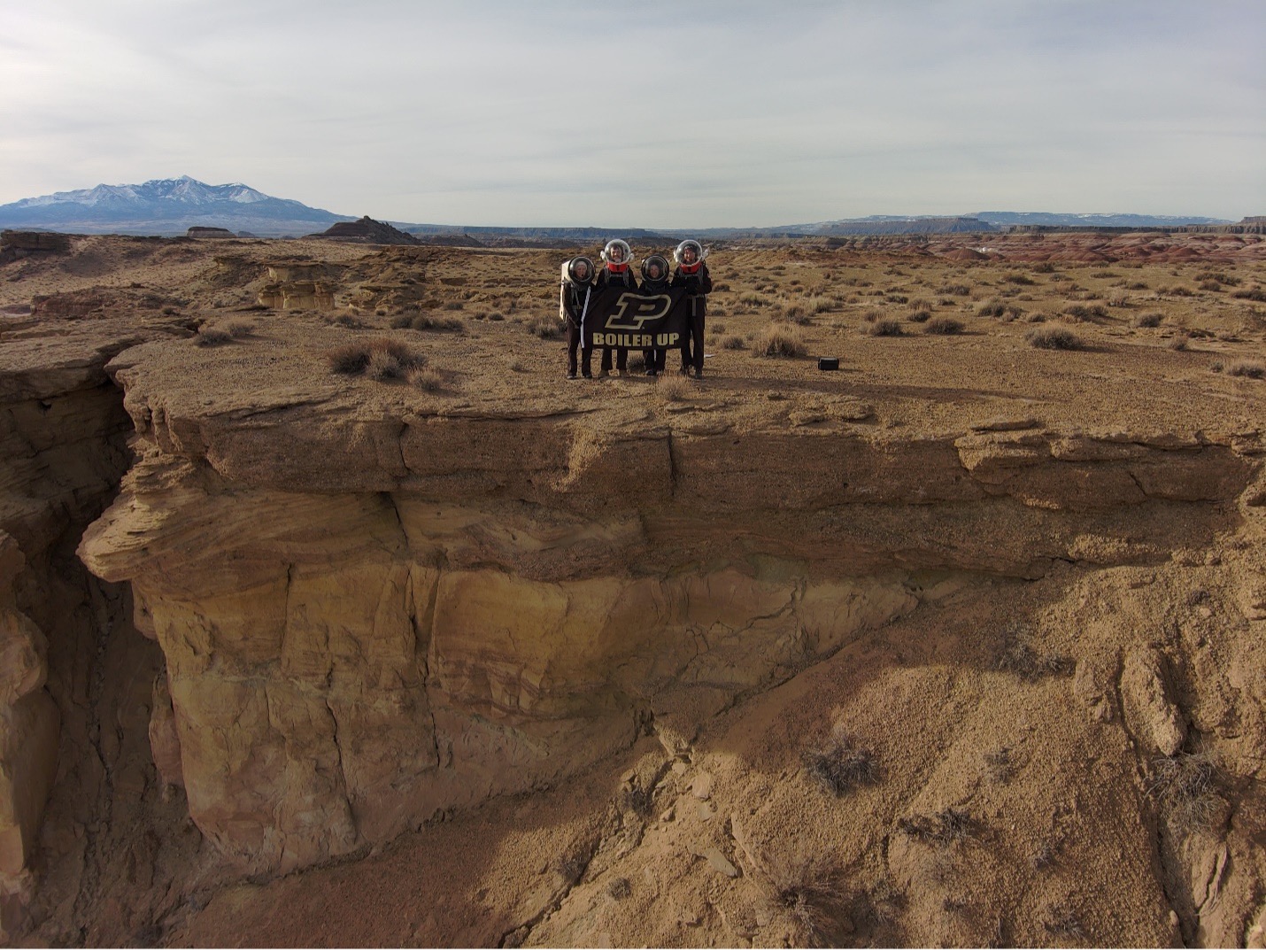 Students in simulated space suits holding a Purdue banner in the desert