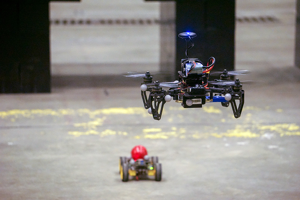 a four-rotor drone following a small RC car with a red ball on top