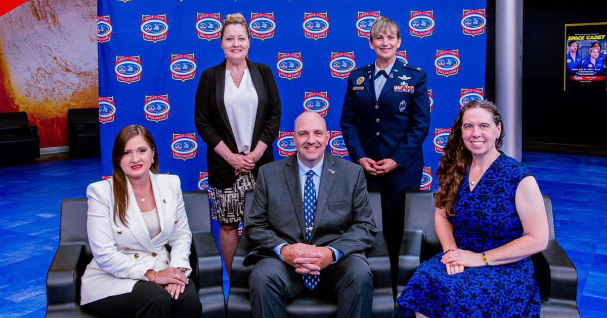 Five people standing and sitting in front of a photo backdrop