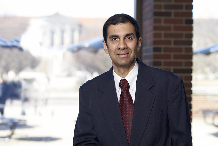 Professor Anand Raghunathan stands in the atrium of the MSEE building. He is wearing a black suit and a red tie.