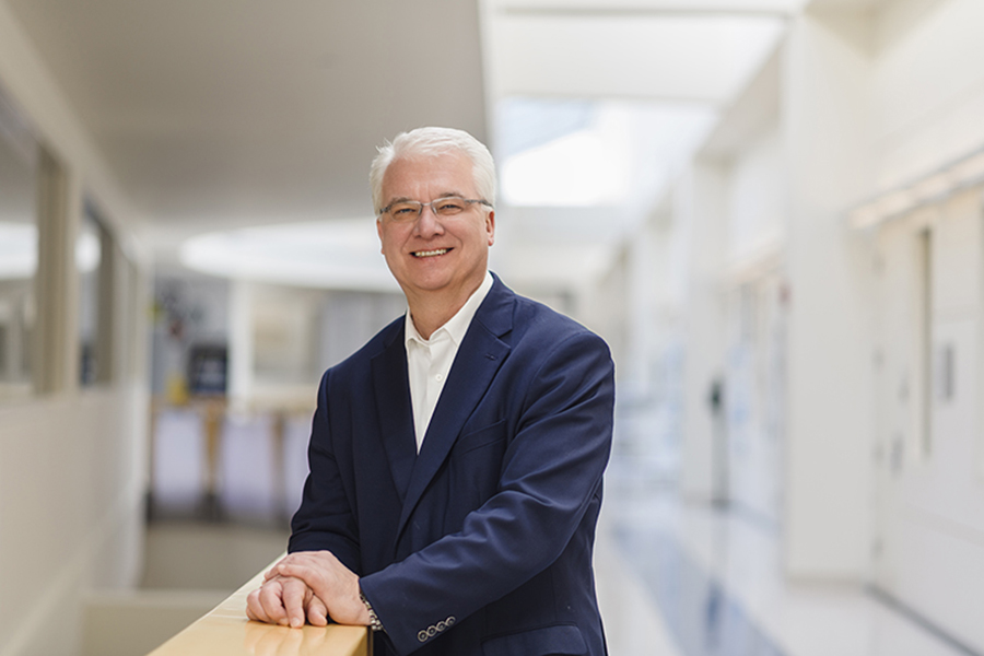 Professor Joerg Appenzeller stands in the hallway of the convergence center. He is wearing a black suit.