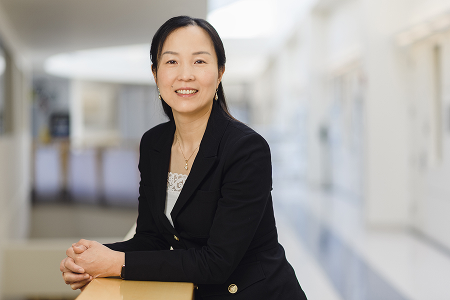 Zhihong Chen poses for a photo while leaning on a railing in the Birck Nanotechnology Center. She is wearing a white shirt and a black suit.