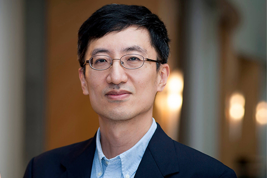 Portrait of Y Charlie Hu taken in the atrium of the MSEE building. He is wearing a light shirt, suit jacket, and glasses.