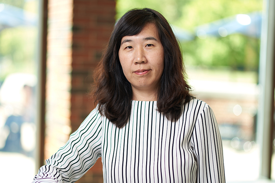 Portrait of Jing Gao. She is wearing a striped top and standing in front of the windows in the atrium of MSEE.