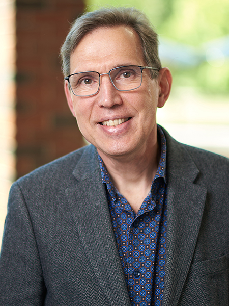 Professor Alexander Kildishev is posing for a portrait in the atrium of the MSEE building. He is wearing glasses, a blue button up shirt, and a suit jacket.
