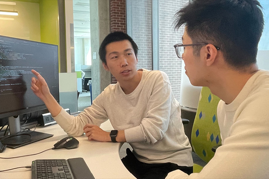 Two men at a table, engaged in discussion while looking at a computer screen.