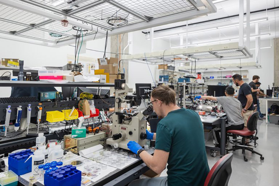 People working in robotics workspace. Man in forefront looking into microscope.