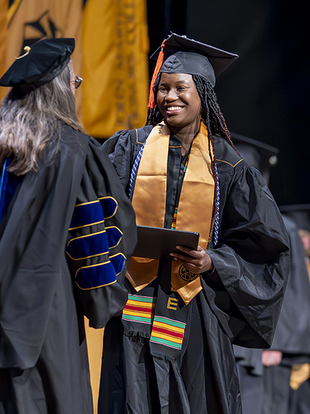 Student in cap and gown, smiling, receiving diploma, shaking hands