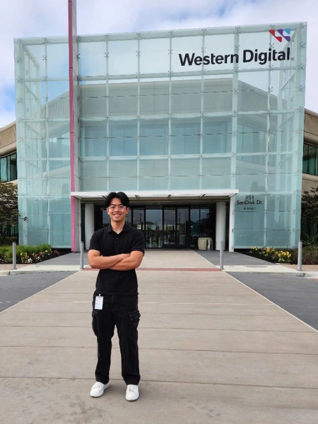 Student wearing glasses, smiling, in front of a building with a glass side that says "Western Digital."