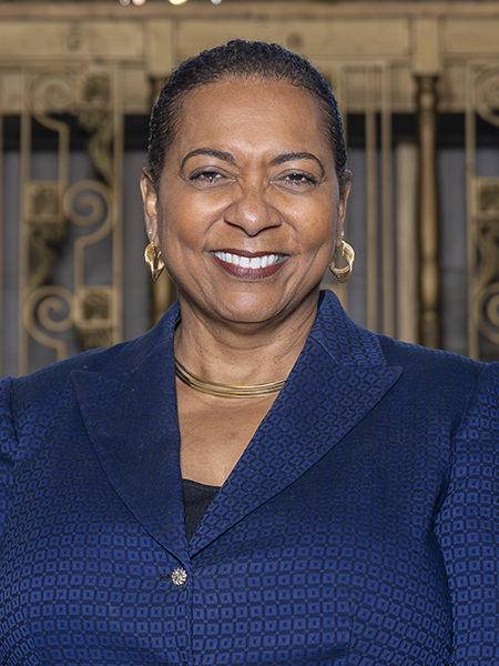 Woman smiling, wearing blue blazer, gold earrings and necklace