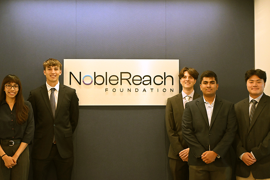 Five students standing in front of a wall, painted blue, with "NobleReach Foundation" on it