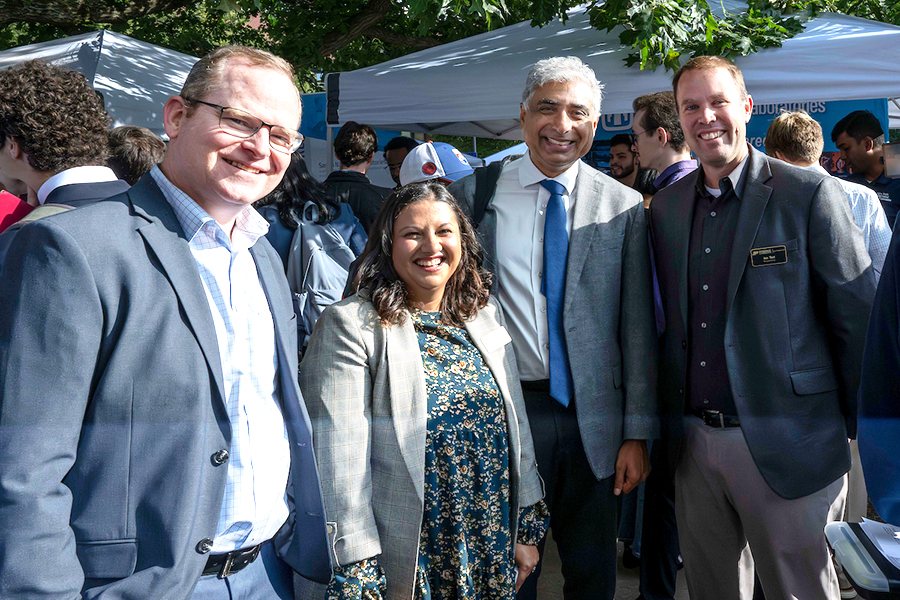 Group of four people, smiling, posing for photo, standing among the tents at Industrial Roundtable
