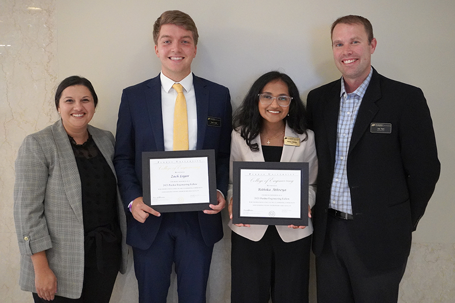 Woman in gray jacket with two students holding award certificates and man with dark blazer, all smiling 