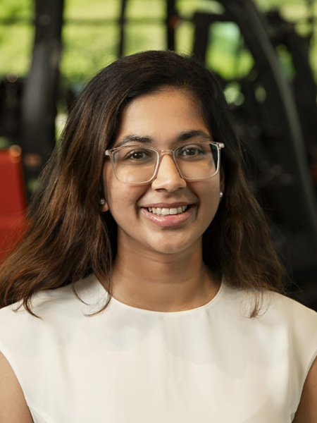 Student with dark hair, glasses, smiling, wearing white blouse
