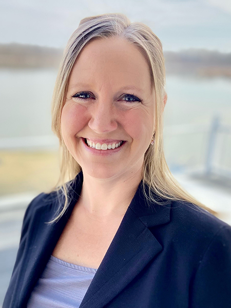 Head shot of woman with blonde hair and blue eyes, smiling, wearing navy blazer