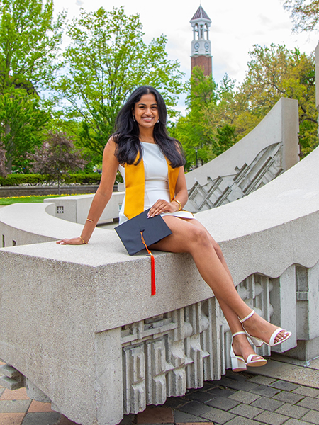 Student in a white dress, long dark hair, smiling, sitting near the engineering fountain