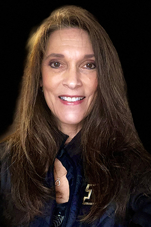 Woman with long brown hair and brown eyes, smiling, wearing a black zip-up with a motion "P" on chest