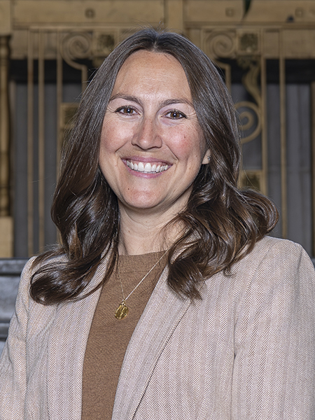 Woman with dark brown hair and brown eyes, smiling, wearing tan blazer